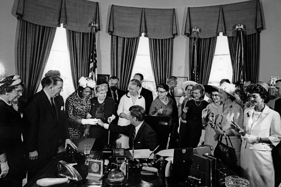 Black and white photo of a group of women and men around a desk